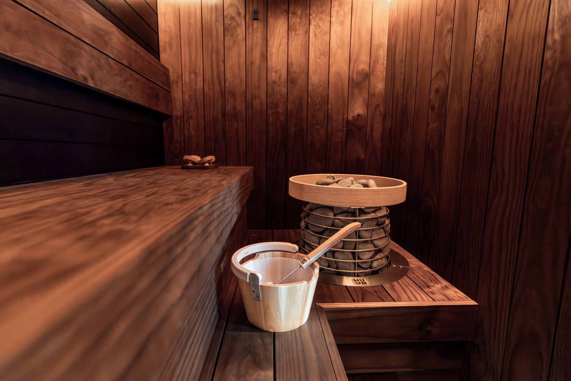 Sauna interior, empty and quiet, with heater, rocks and a wooden bucket on the bench