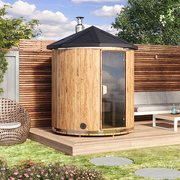 VIRU Vertical standing barrel sauna on a garden terrace beside a lounge set, full-height glass door
